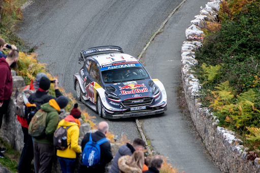 A rally car rounding the corner in front of spectators.