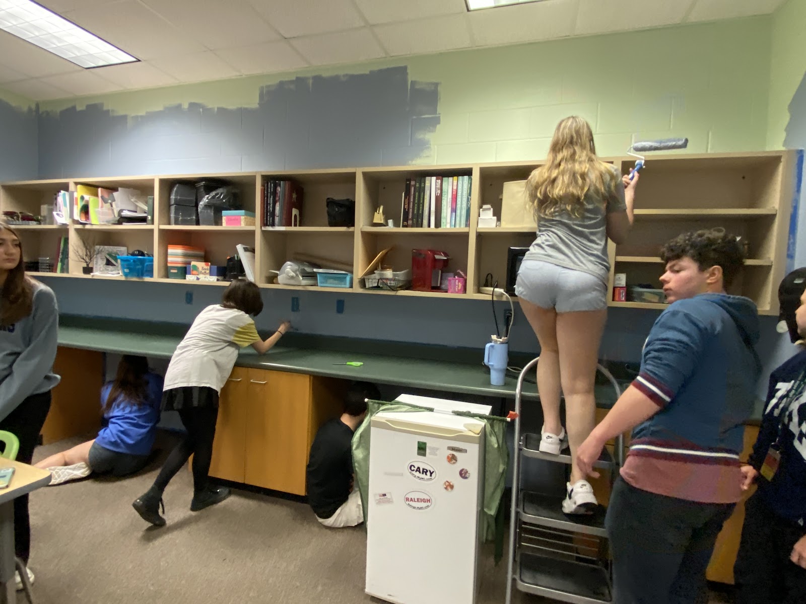 Interior design students use a variety of brushes to paint the walls of the old storage room a new shade of blue. They work together to ensure no spot of green is left unchecked.