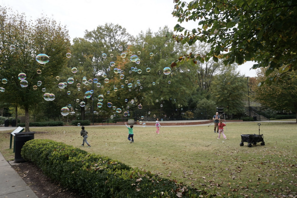 A picture of Pullen Park featuring a man blowing bubbles while a group of kids chase after them. 
