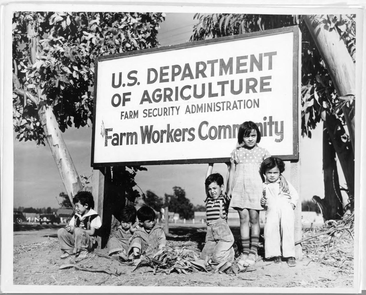 A group of children pose under a sign at the USDA’s Farm Workers Community. Photo used with permission by Robert Hemming (Library of Congress).
