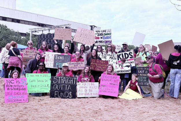 Protesters gathered behind the speakers in Raleigh with signs calling for increased pay for teachers and school funding.