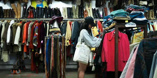 An image depicting a woman looking at clothes inside a thrift store. Image used with persimmon by Kiko Camaclang on Unsplash.